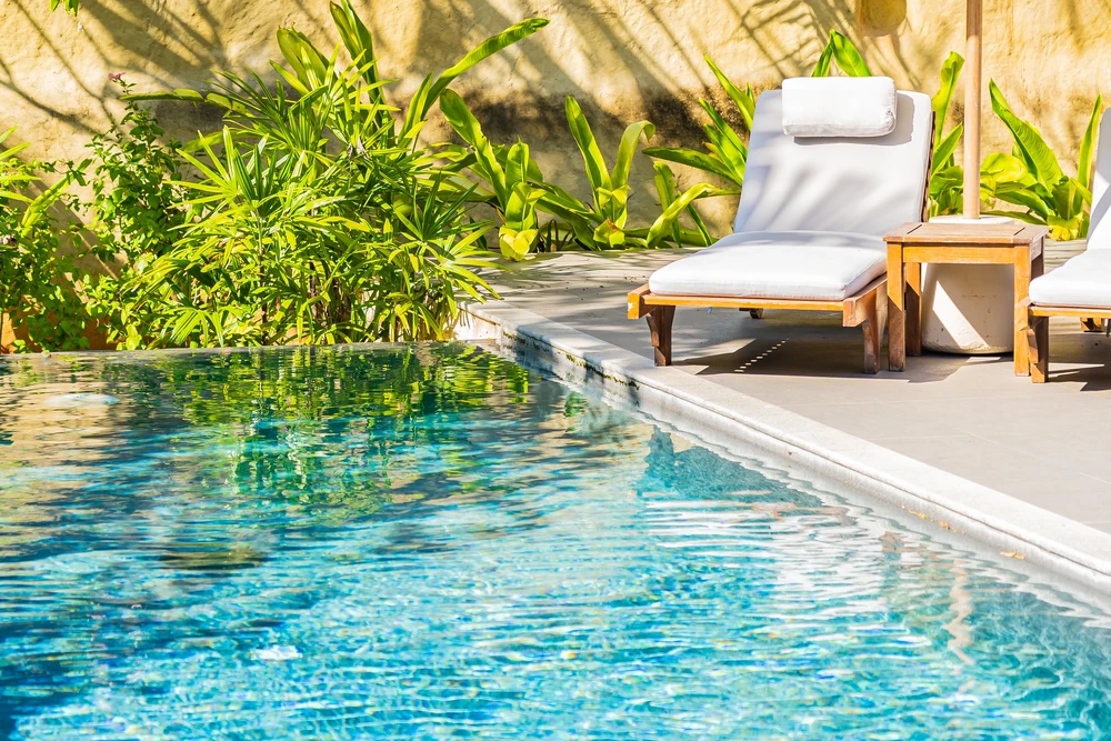 Scène extérieure au bord d'une piscine carrelée bleue avec margelles en composite marron