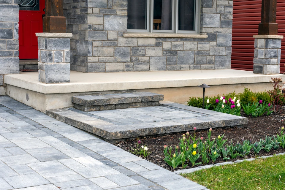 Aménagement paysager extérieur résidentiel avec escaliers en pierre naturelle multicolore, terrasse surélevée en dalles beiges et marches intermédiaires